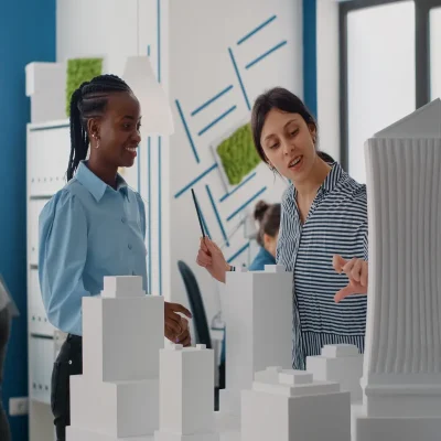 Profissionais analisam maquete no mercado de administradoraDuas profissionais discutem maquetes em escritório, representando inovação e crescimento no mercado de administradora de condomínios e suas oportunidades.