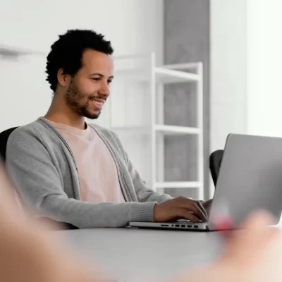 Um homem sorridente está utilizando o software Abas em um laptop, enquanto trabalha em um ambiente descontraído.