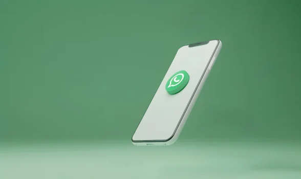 Smartphone branco inclinado com o logotipo verde do WhatsApp em 3D centralizado na tela, em um fundo verde suave. A imagem representa a ferramenta de comunicação mais utilizada, o WhatsApp em condomínios, destacando sua popularidade e agilidade, mas também a necessidade de regras claras e moderação. A utilização profissional e segura requer o estabelecimento de limites legais e práticos e a consideração de alternativas especializadas como o Group COM.