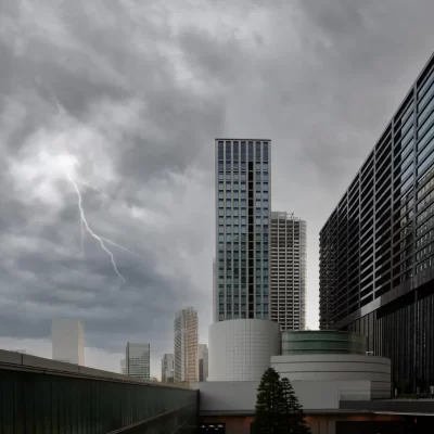 Uma cidade com prédios altos sob um céu nublado, onde um relâmpago é visível, ilustrando a necessidade de manutenção de para-raios para segurança das construções.