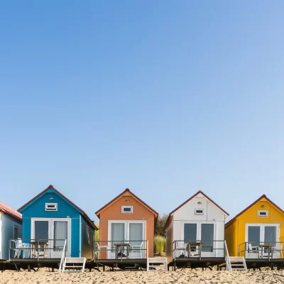 Casas coloridas para aluguel de temporada à beira da praia, com varandas voltadas para o mar sob um céu azul.