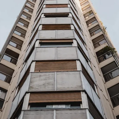 Edifício residencial moderno visto de baixo, simbolizando a estrutura do condomínio. A cota condominial é o valor mensal essencial para custear despesas coletivas, manutenção e serviços (como segurança e limpeza), garantindo o equilíbrio financeiro da gestão. O cálculo da cota condominial é feito por meio de rateio com base na previsão orçamentária.