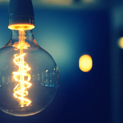 Lâmpada incandescente ligada em fundo escuro, simbolizando economia e luz. A energia elétrica por assinatura para condomínios é um modelo sustentável que oferece créditos de energia renovável, gerando economia na conta de luz (até 15%) e previsibilidade de custos. O serviço de energia elétrica por assinatura dispensa obras ou instalação de painéis solares.
