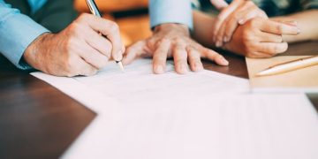 Imagem de uma pessoa assinando um papel, a fim de representar o tema tipos de contratos em shopping.