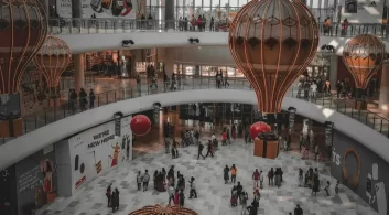 Shopping decorado com balões e caixas de presente, ilustrando ações promocionais e estratégias de marketing financiadas pelo Fundo de Promoção e Propaganda.