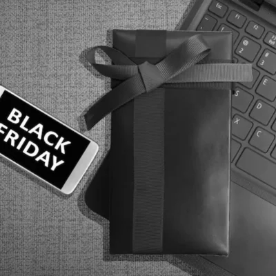 Celular com a frase “Black Friday”, presente embrulhado e notebook, simbolizando oportunidades da Black Friday para administradoras