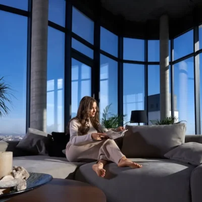 Mulher relaxando em sofá moderno dentro de apartamento com grandes janelas de vidro em um condomínio-clube.