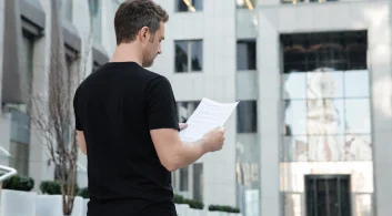 Síndico morador lendo documento em frente ao prédio