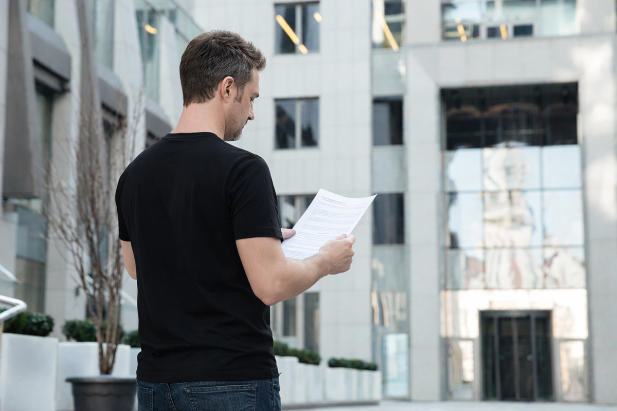 Síndico morador lendo documento em frente ao prédio