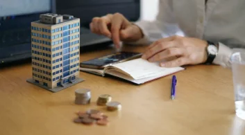 Mesa com moedas e maquete ilustrando cobrança garantida